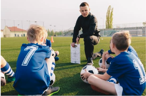 A youth soccer coach kneels to address players